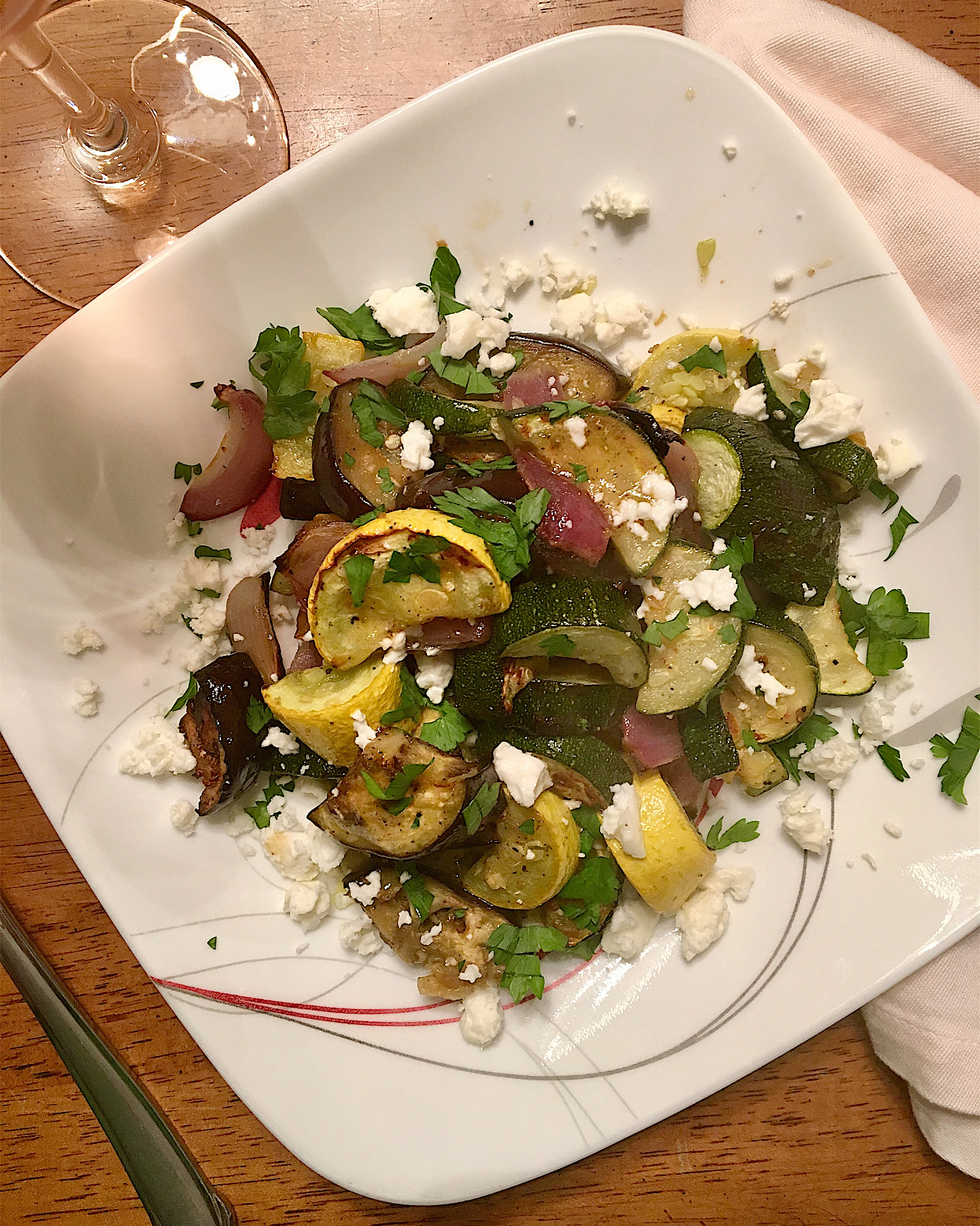 Roasted yellow squash, zucchini, eggplant, and red onion piled on a white plate, drizzled with red wine vinaigrette and sprinkled with feta cheese and parsley.